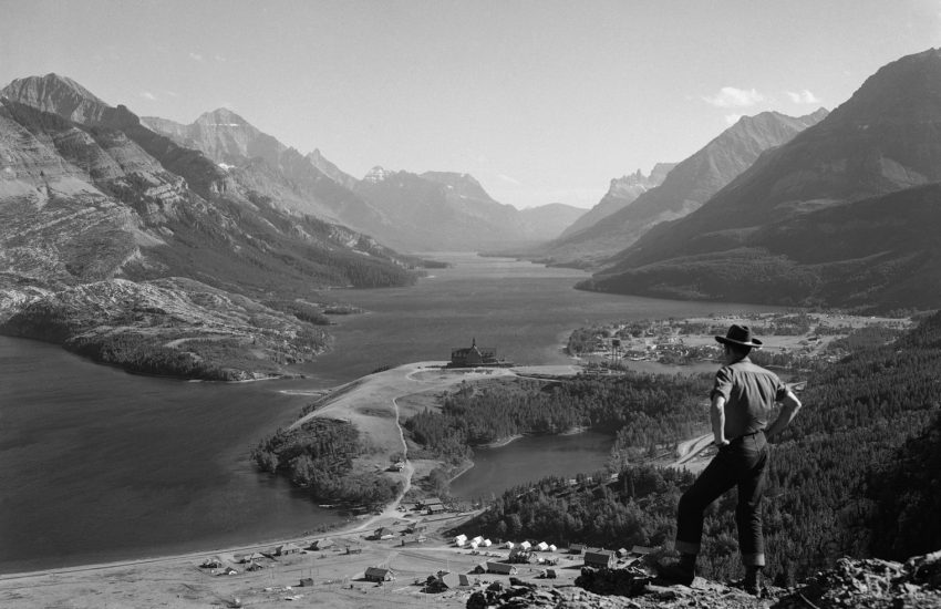 a man standing on top of a mountain next to a lake